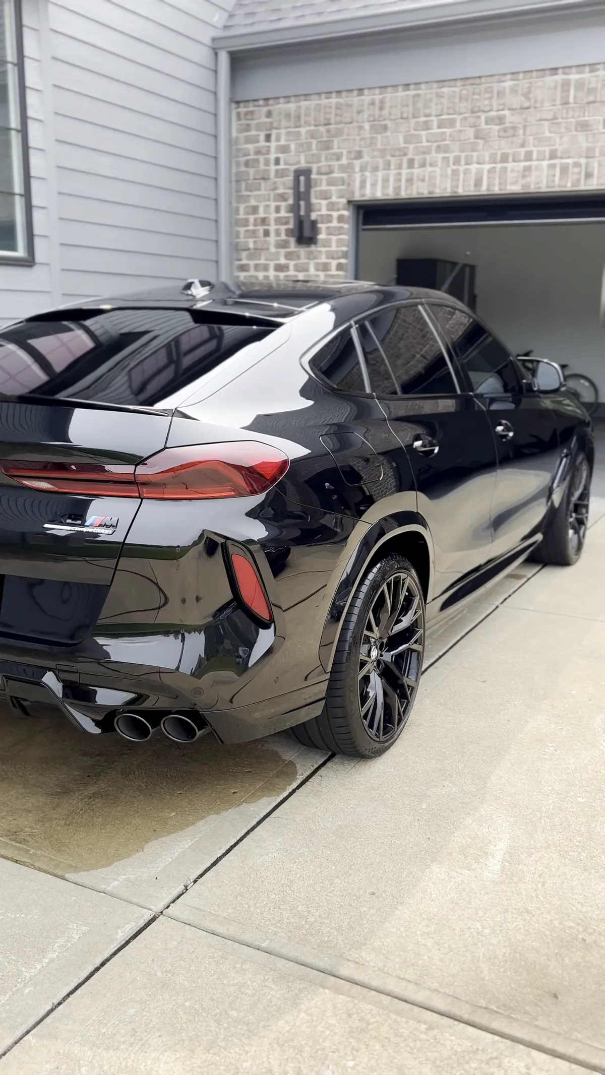 Freshly detailed black BMW X6 M, its glossy paint mirroring the house and sky