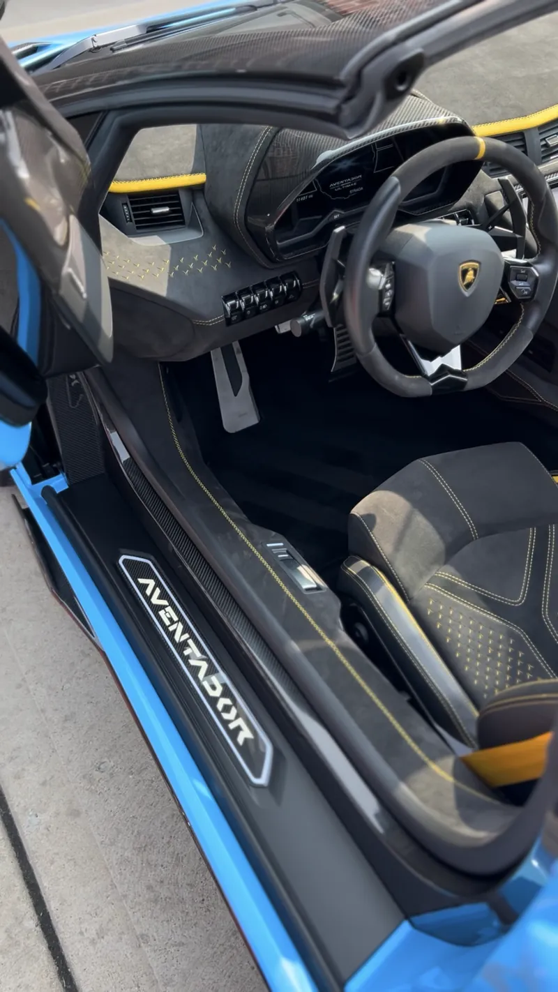 Open scissor door of a blue Lamborghini Aventador showing a cleaned Alcantara cabin with yellow stitching